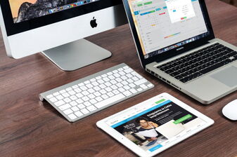 Foto mit Desktop-Bildschirm, Tablet und Laptop, die auf einem Holztisch stehen