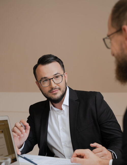 Kunde und Dienstleister sitzen am Tisch, wo ein Notebook zu sehen ist.