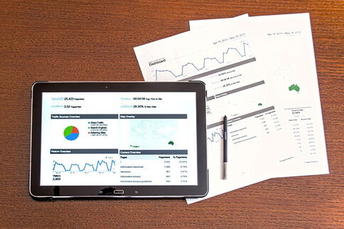 Tablet mit Tortengrafik auf Tisch liegend, halb darunter 2 Blätter mit verschiedenen Grafiken