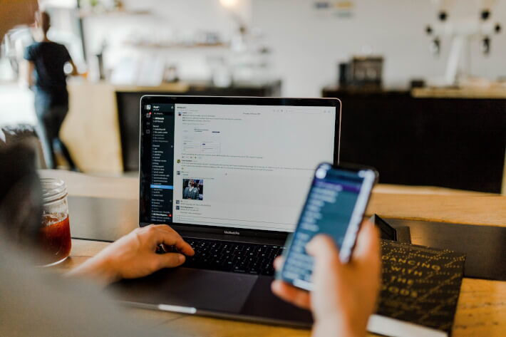 Mann arbeitet am Laptop und hat Smartphone in der rechten Hand