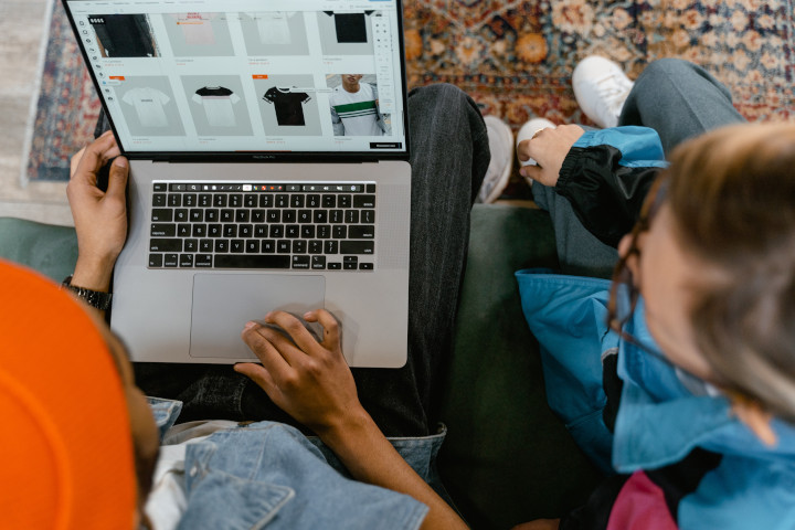 Modeshop Mann links und Frau rechts schauen sich am Laptop auf der Couch T-Shirts im Webshop an