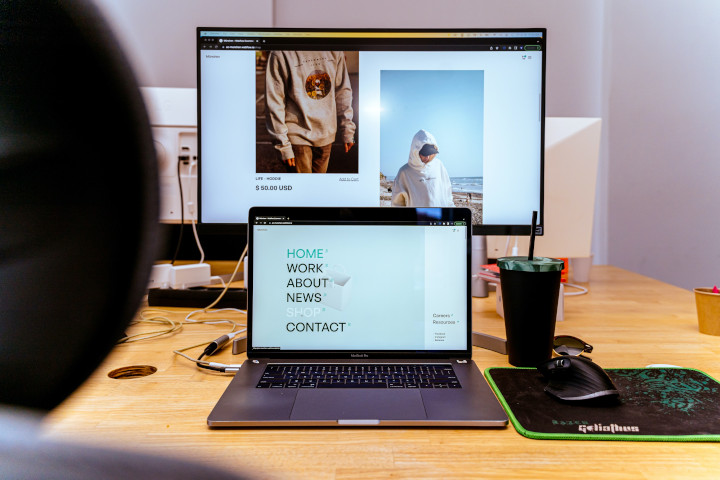 Onlineshop Entwicklung Desktop mit zwei Produktbildern die einen Pullover und weiße Jacke mit Kapuze zeigen, davor ein Laptop mit der Startseite des Webshops.