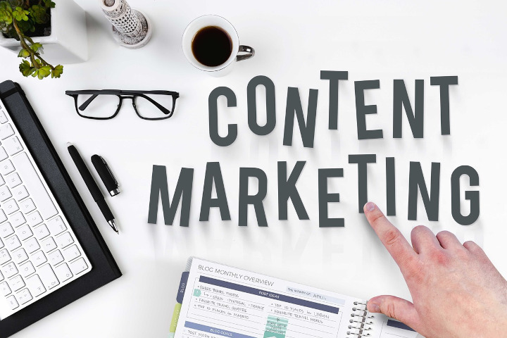Content Marketing liegen in Buchstaben auf weißem Tisch, links daneben eine Brille, ein Kugelschreiber und eine PC-Tastatur.