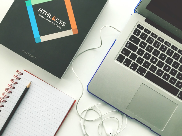 HTML und CSS Fachbuch, Notebook und Schreibblock liegen auf Tisch